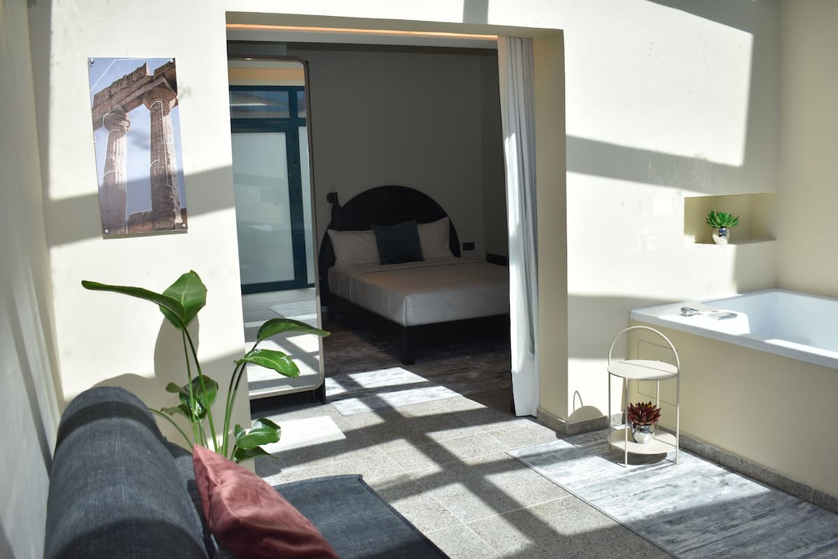 A modern hotel room with a bed, a small bathroom, and a view of the outside.