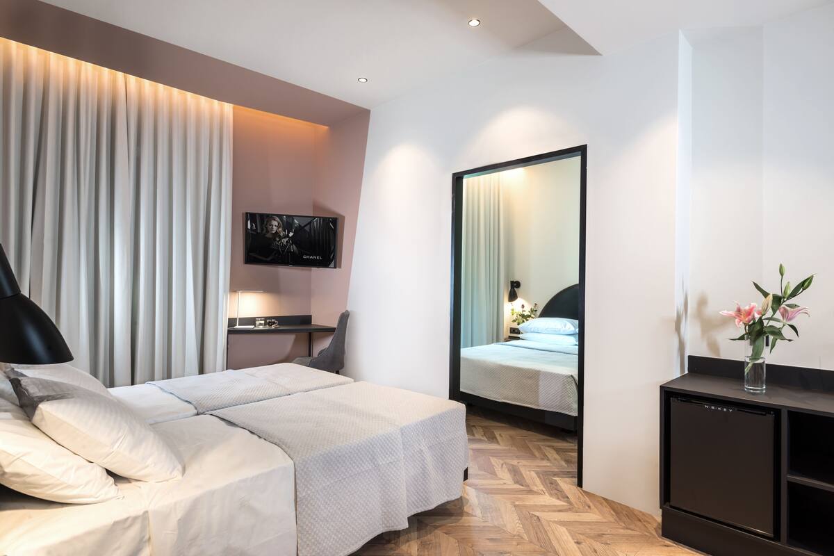 A modern hotel room with a bed, a desk, a flat-screen TV, a mirror, and a small cabinet.