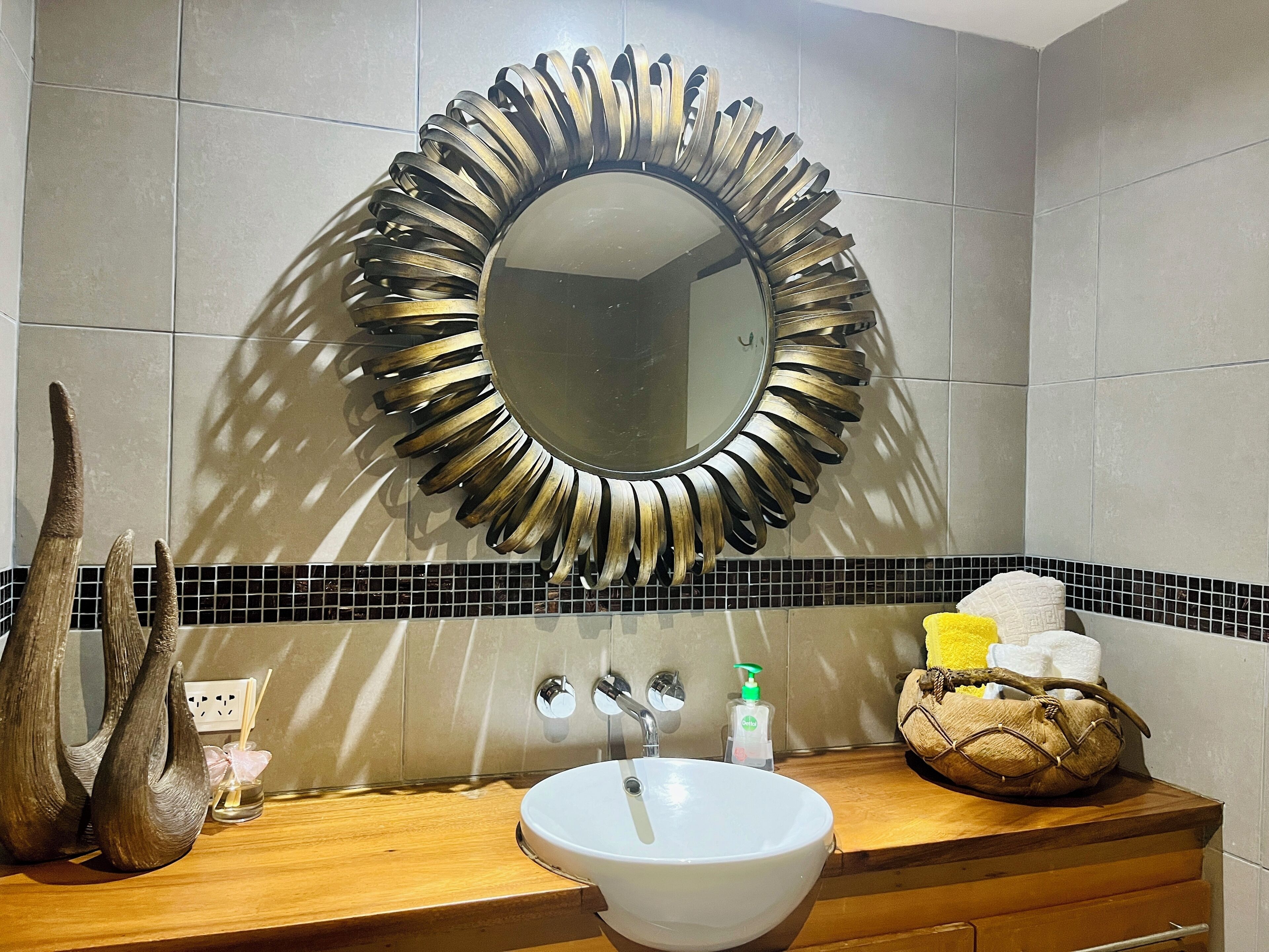 A bathroom with a round mirror, wooden countertop, white sink, and decorative items.