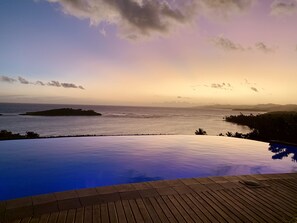 Ein Pool ohne Ende mit Blick auf das Meer und ferne Inseln im Sonnenuntergang.