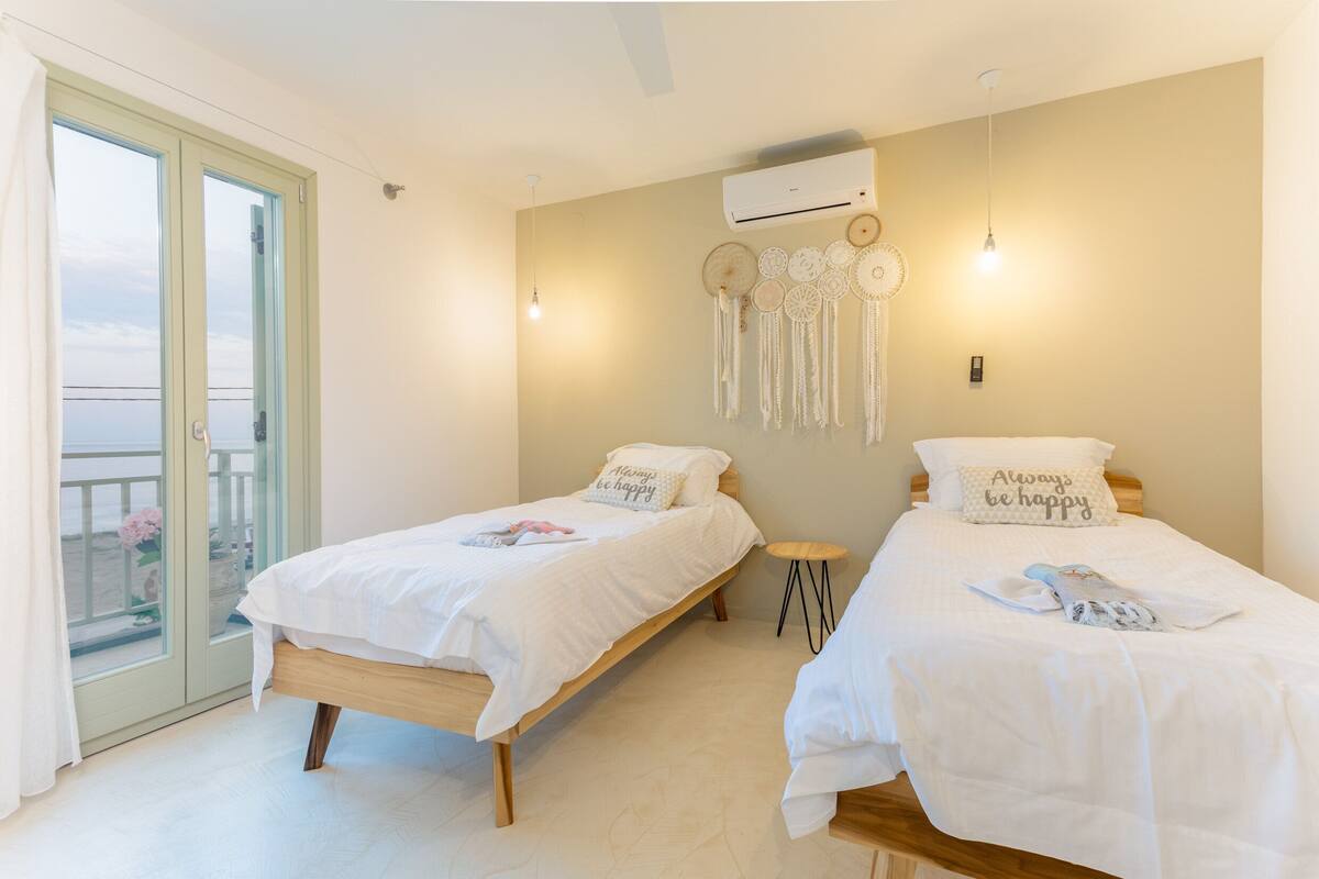 A room with two beds, a balcony, and a wall-mounted air conditioner.