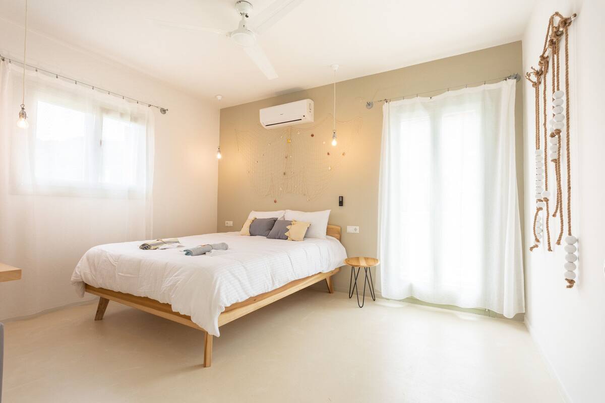 A bedroom with a wooden bed, white bedding, a small stool, and a ceiling fan.