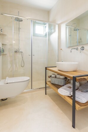 Une salle de bain moderne dotée d’une douche à parois de verre, d’une baignoire blanche sur pieds et d’un meuble-lavabo en bois, avec un grand évier et des étagères pour les serviettes.