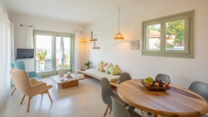 A modern living room with a sofa, chairs, a dining table with fruit, and a TV. - Sea and Sun Luxury Pools' Villas (Zagora-Mouresi)
