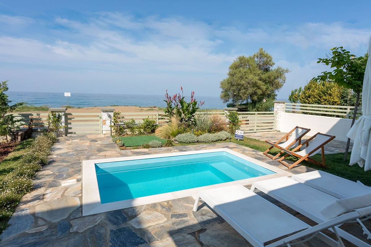 A pool area with lounge chairs, a stone pathway, and a view of the sea.