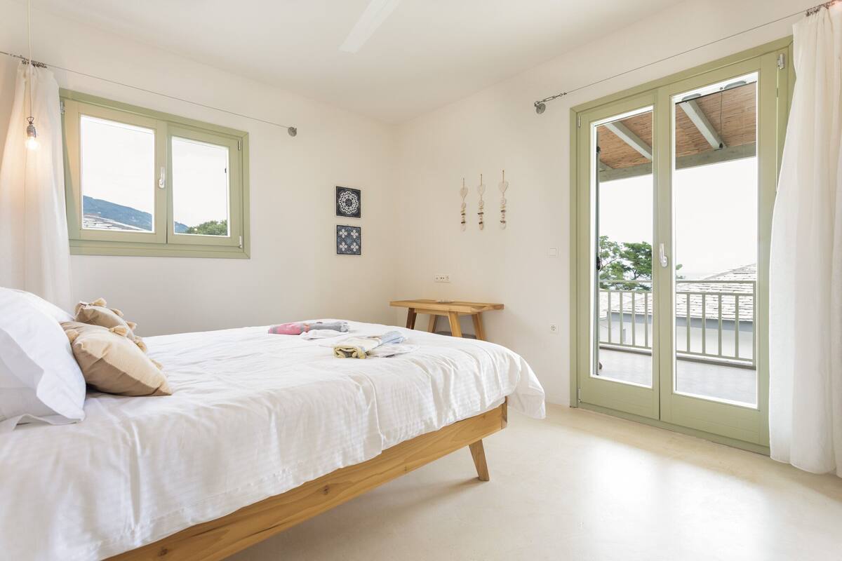A bedroom with a bed, a small table, and a window with a view of the outside.