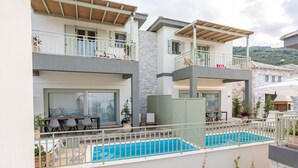 A modern two-story building with a swimming pool, outdoor seating, and a stone facade. - Sea and Sun Luxury Pools' Villas (Zagora-Mouresi)