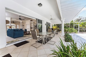 A covered patio with a dining table and chairs, a blue sofa, and a ceiling fan.