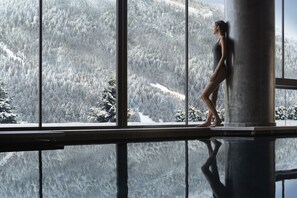 A person standing by a window overlooking a snowy forest.