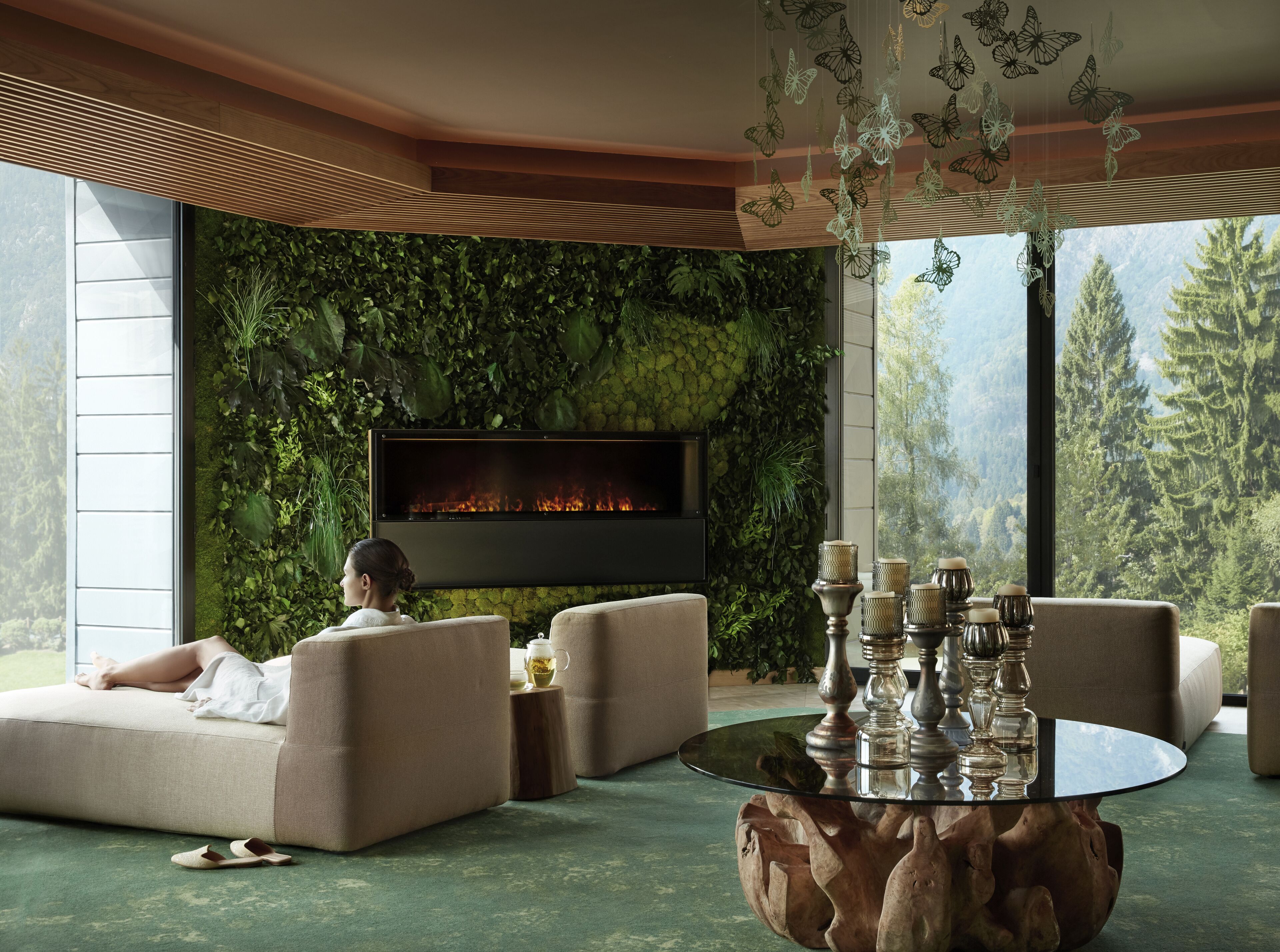 Ein modernes Wohnzimmer mit Kamin, bequemen Sitzmöglichkeiten und einem großen Fenster mit Blick auf einen Wald.