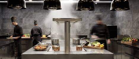 Una cocina moderna con electrodomésticos de acero inoxidable, lámparas colgantes negras y una isla central con ollas.