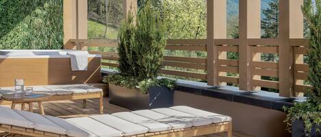 A wooden deck with a cushioned seating area, a grill, and potted plants.