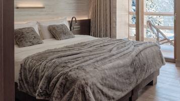 A large bed with a fluffy blanket, a bedside table with a lamp, and a view of a snowy landscape through a window.