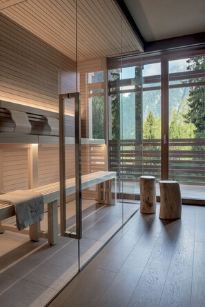 Ein moderner Spa-Bereich mit Holzbänken, einer Glastrennwand und Blick auf eine Berglandschaft.