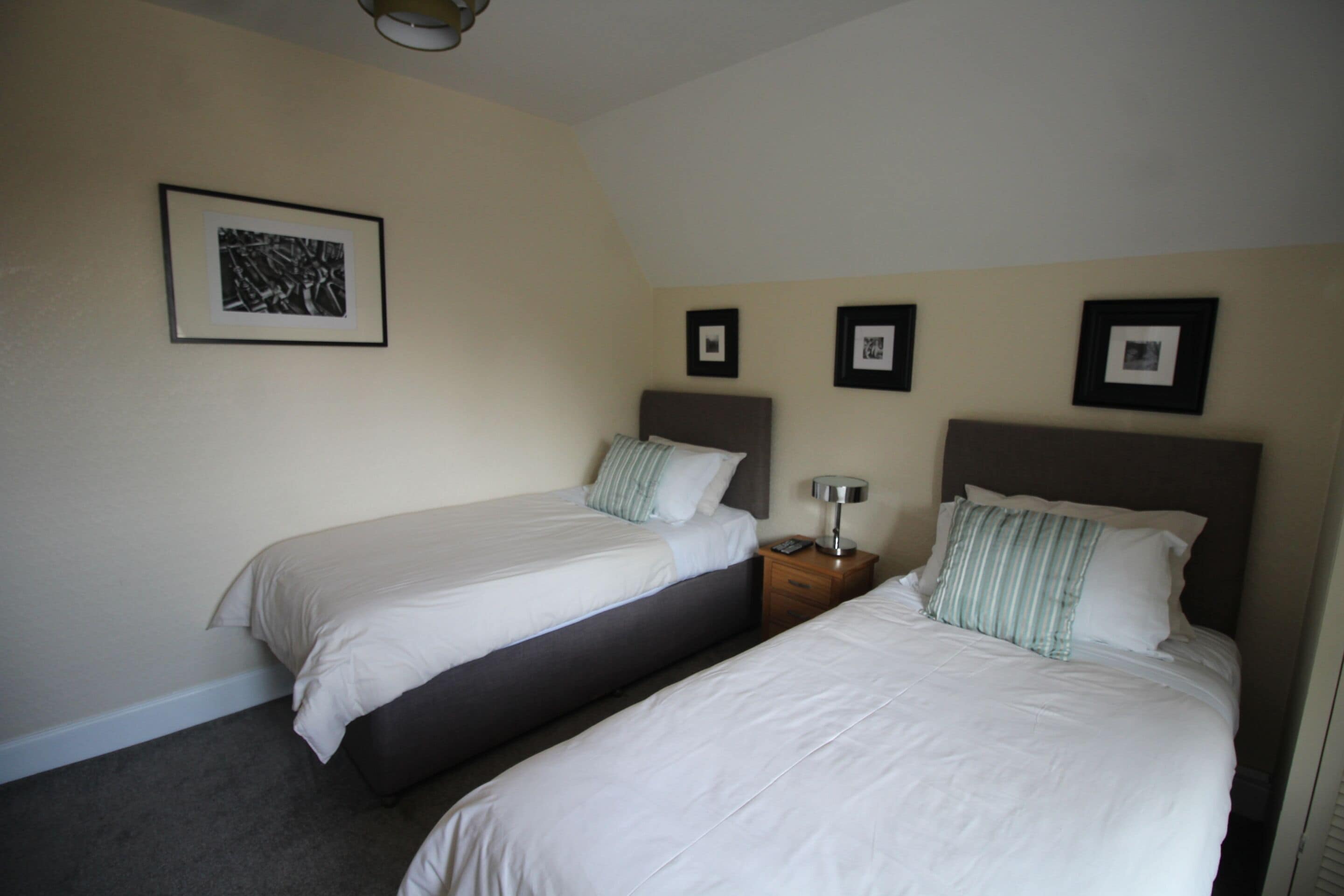 A hotel room with two single beds, a bedside table with a lamp, and a framed picture on the wall.