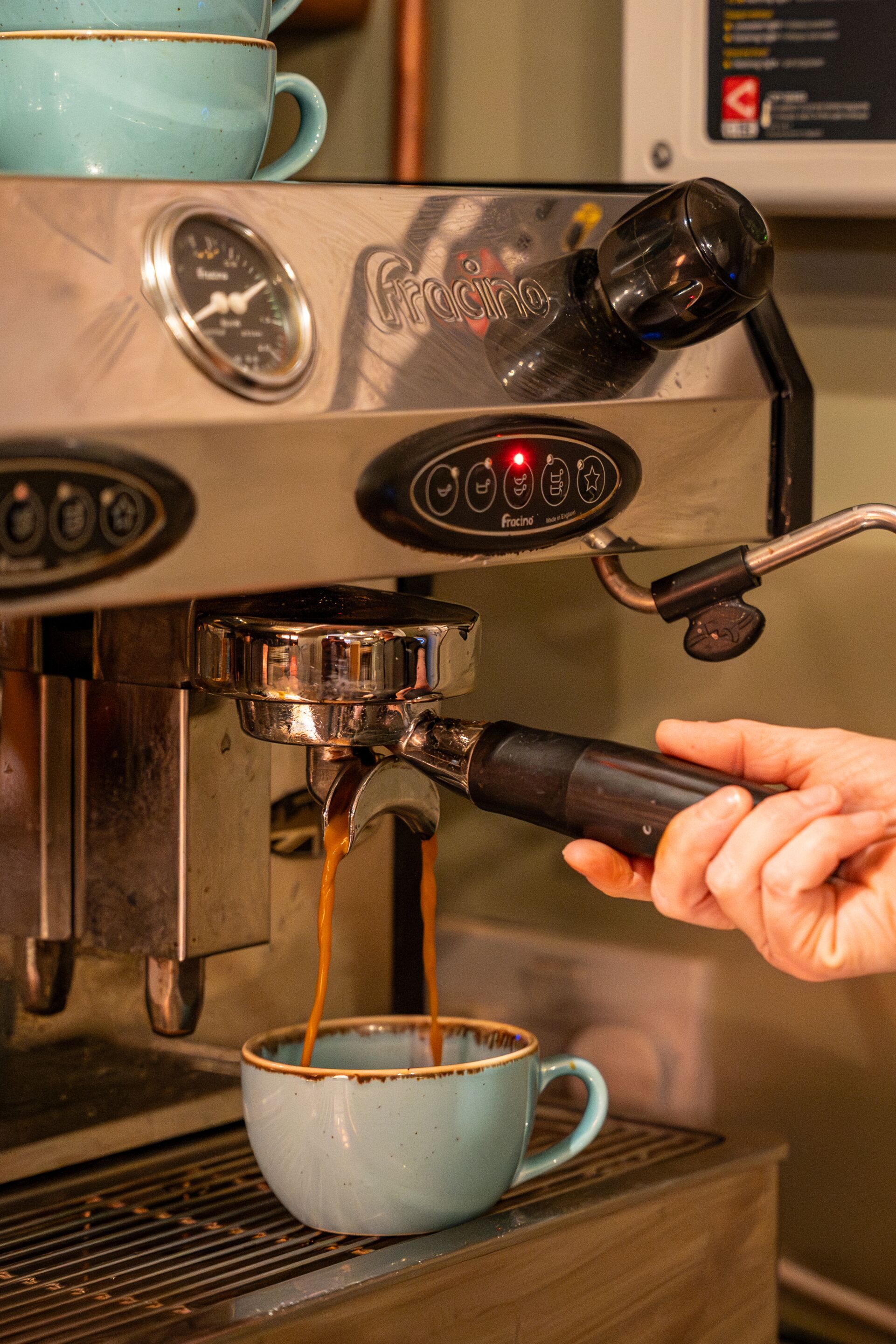 A hand holding a portafilter over a coffee machine, with coffee being dispensed into a blue cup.