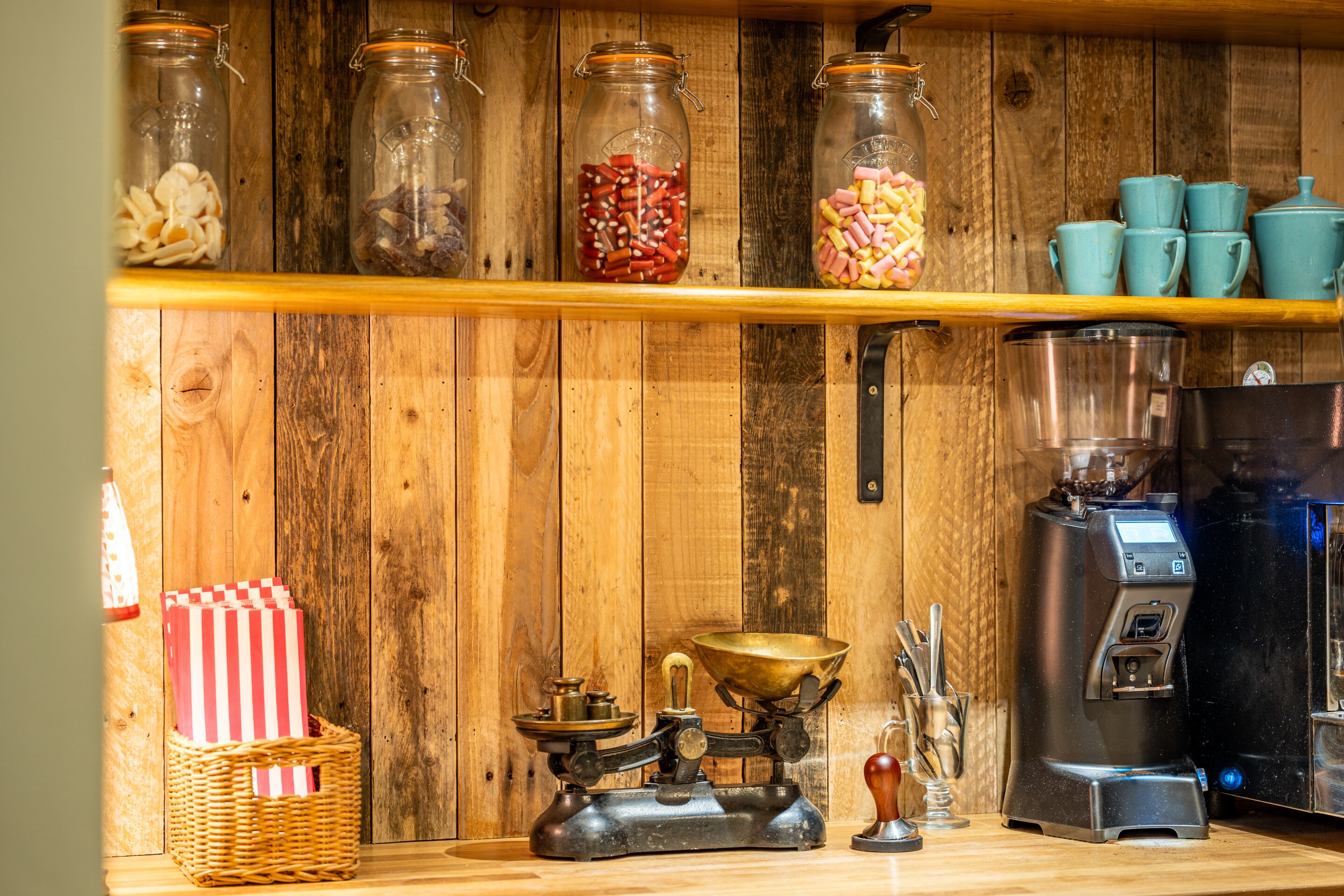 Een keuken met houten planken vol snacks, een koffiezetapparaat en een oude weegschaal.
