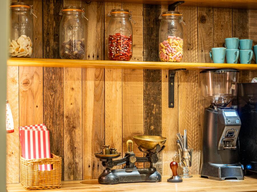 Een keuken met houten planken vol snacks, een koffiezetapparaat en een oude weegschaal.
