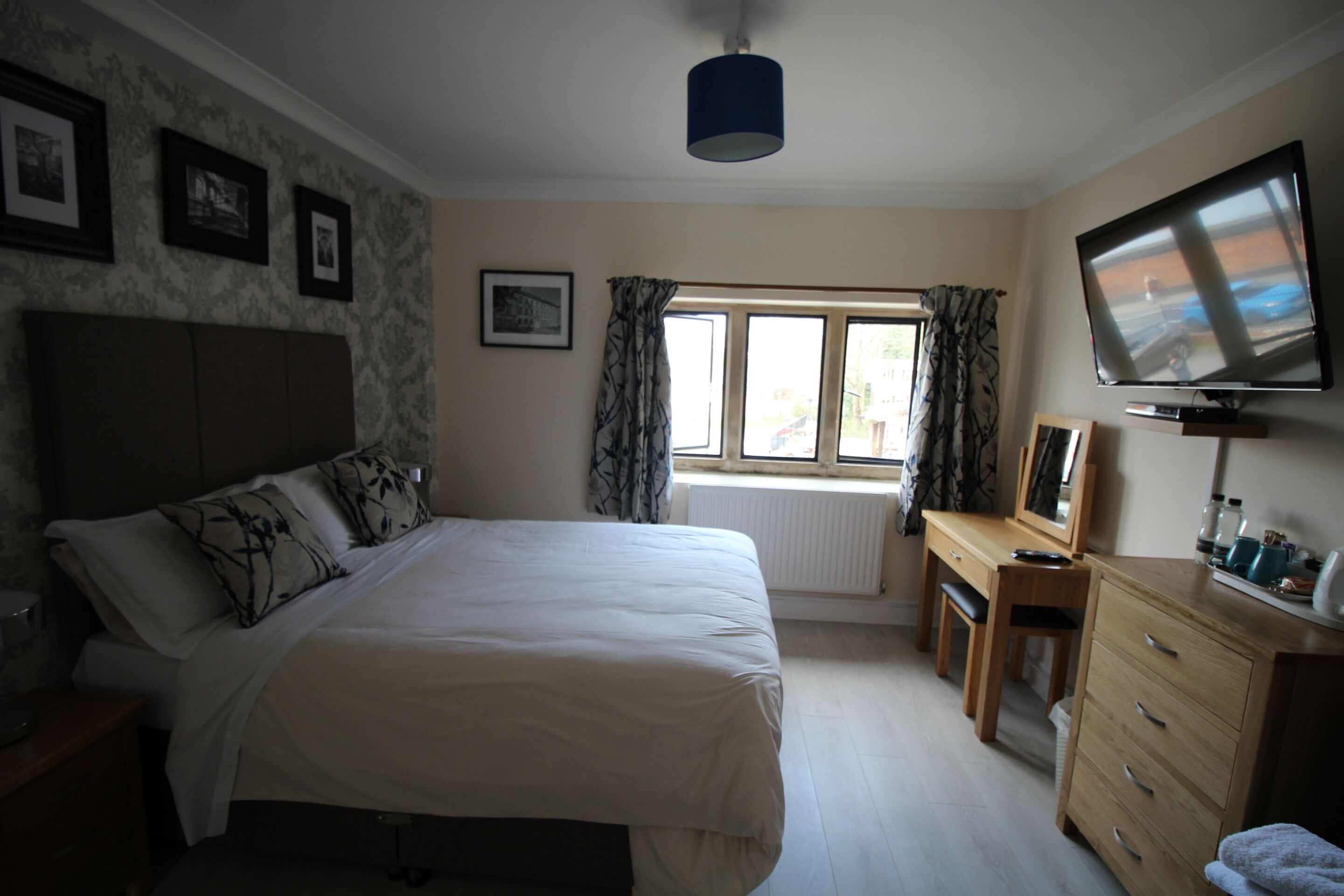 A bedroom with a bed, a desk, a television, and a window with curtains.