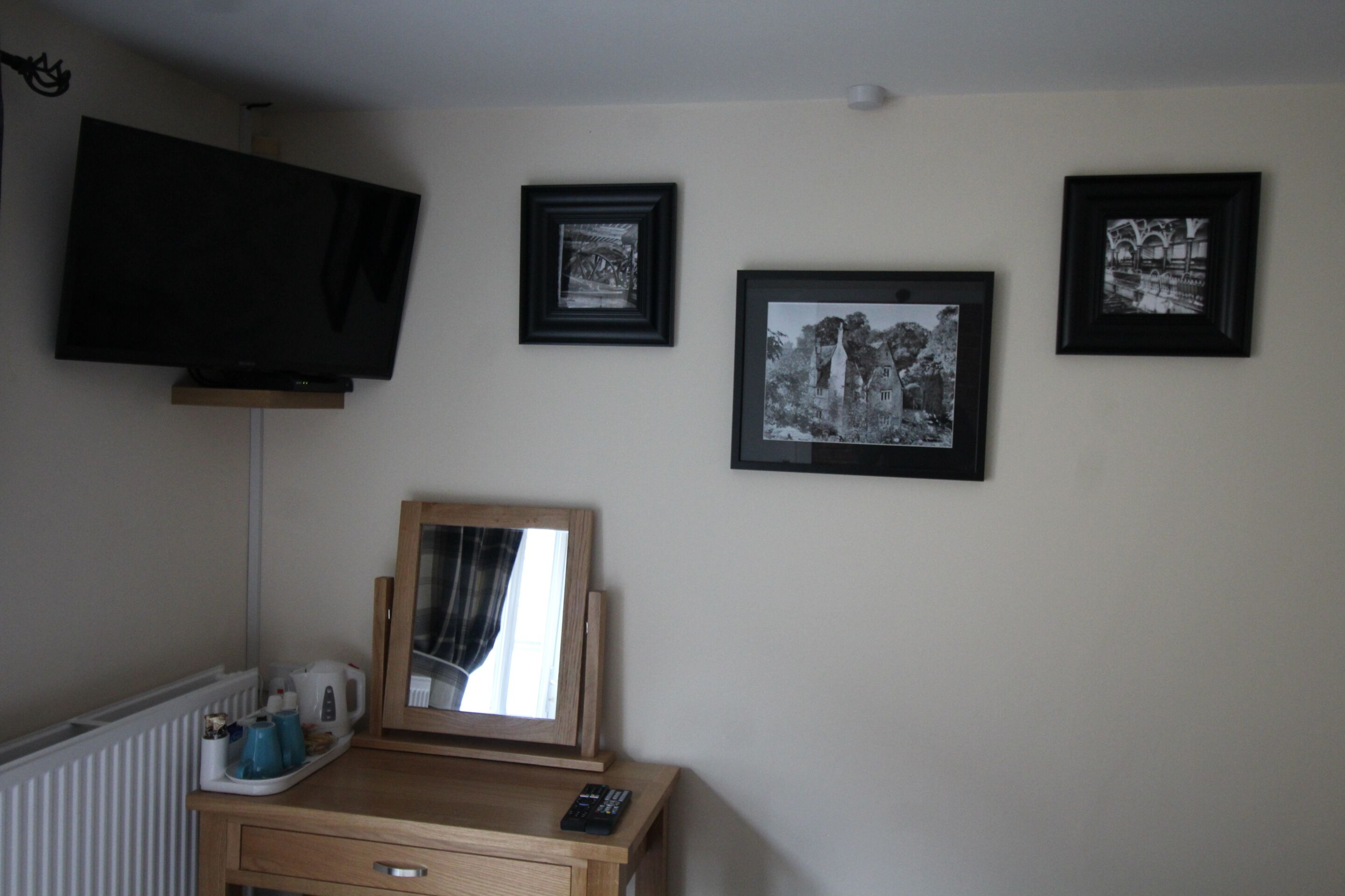 Una habitación con una televisión montada en la pared, un aparador de madera con un espejo y tres cuadros enmarcados.