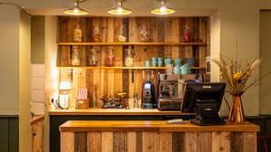 A wooden counter with a coffee machine, jars of snacks, and a vase of dried plants.