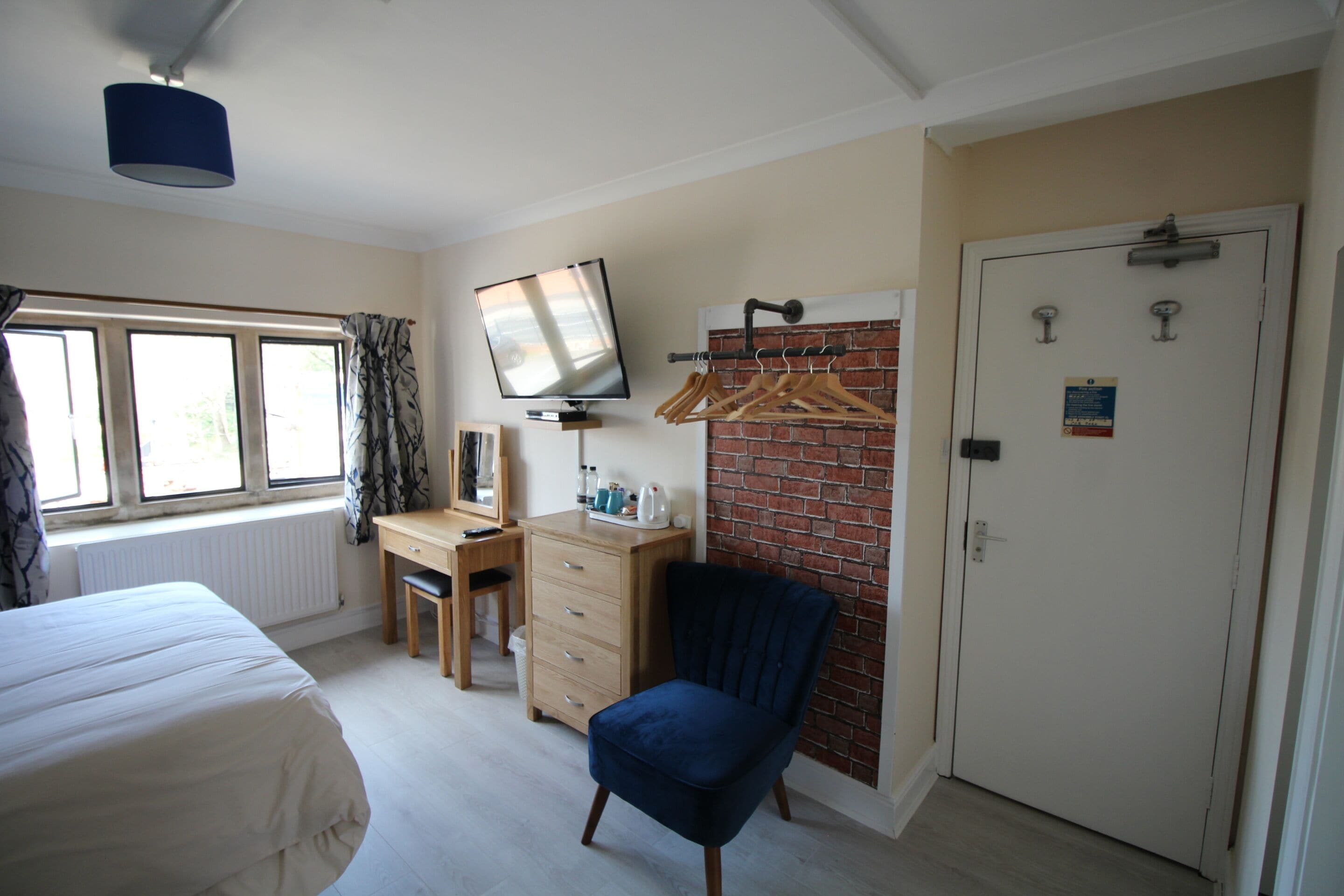 A bedroom with a bed, a desk, a chair, a TV, a wardrobe, and a door.
