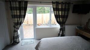 A bedroom with a large bed, a window with curtains, a radiator, and a television on the wall.