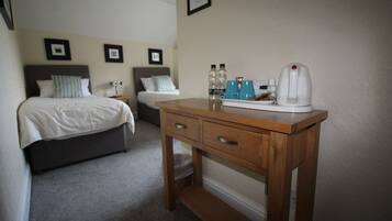 A bedroom with a bed, a wooden nightstand, a desk with a kettle, and two framed pictures on the wall.