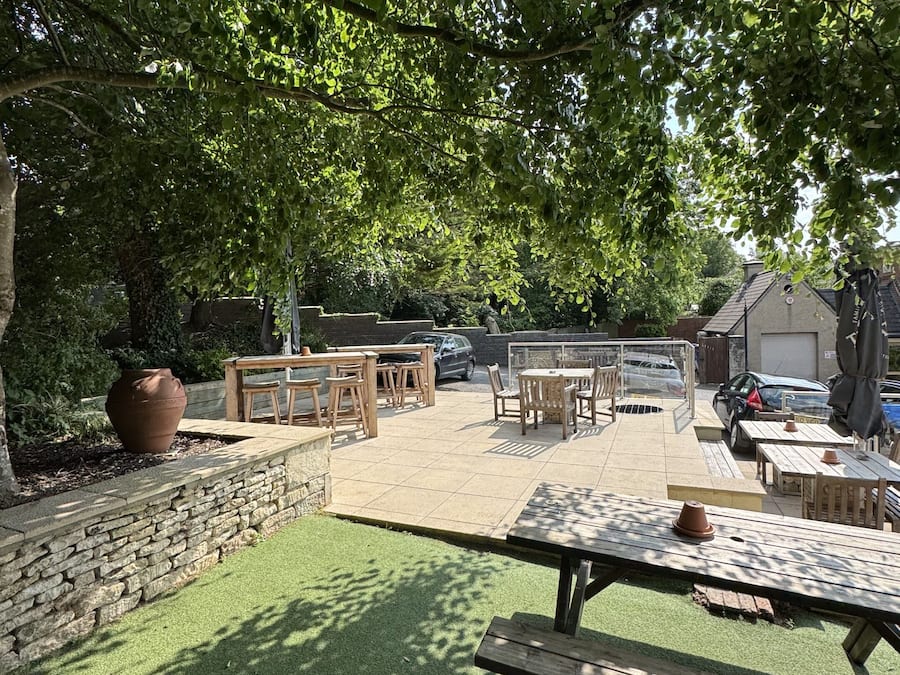 An outdoor patio area with stone walls, a grassy lawn, and wooden furniture.
