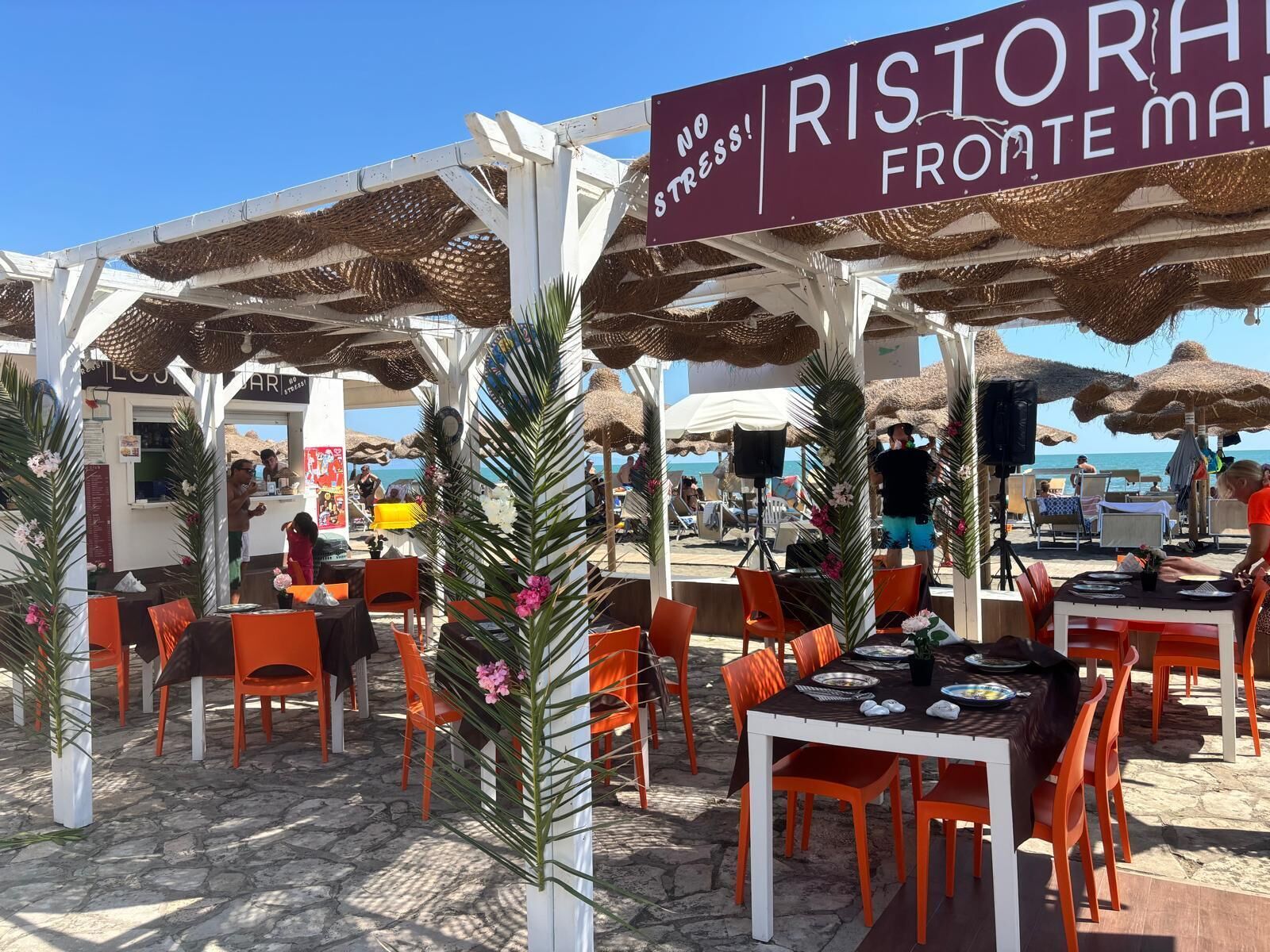 Een restaurant aan het strand met terras, een bord waarop 'RISTORAH FROMATE MARE' staat, en uitzicht op zee.
