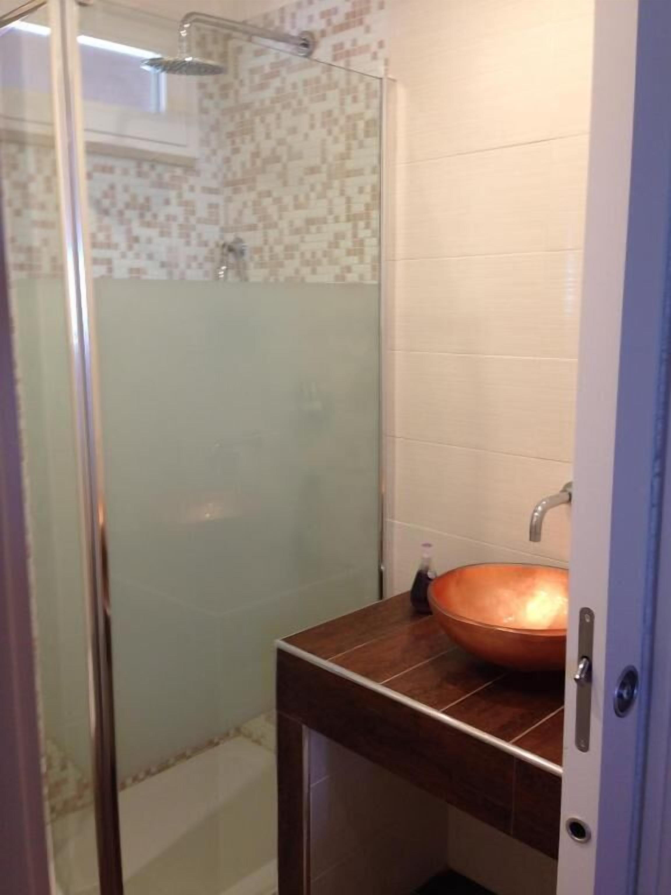 A bathroom with a glass-enclosed shower, a copper sink, and a tiled wall.