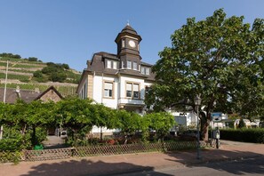 Un edificio con una torre de reloj, rodeado de vegetación y una zona pavimentada.