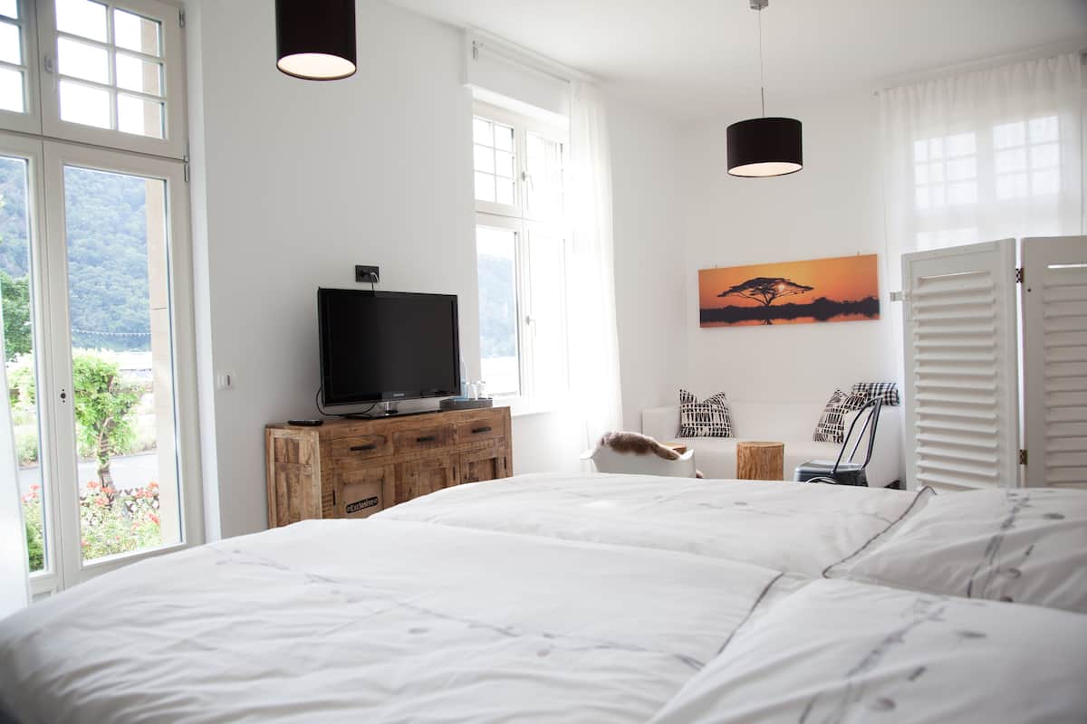 A bedroom with a large bed, a television on a wooden dresser, and a painting on the wall.