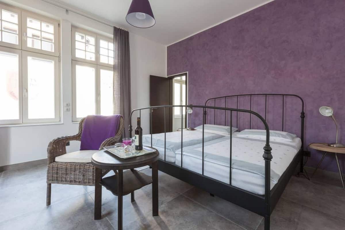 A bedroom with a bed, a chair, a small table, and a window.