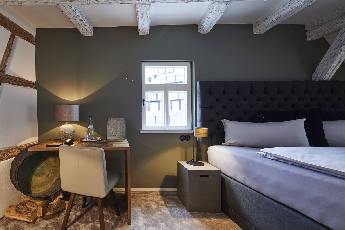 Ett sovrum med en stor säng, ett skrivbord med en stol, en lampa och ett fönster.