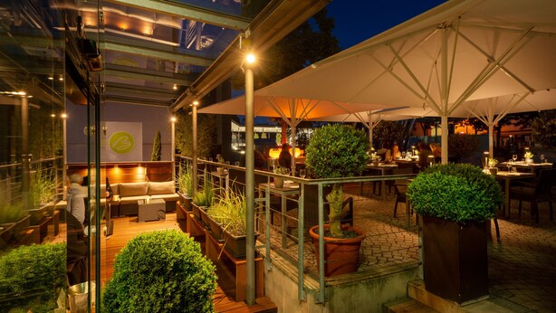 An outdoor patio area with seating, potted plants, and umbrellas providing shade. - Bachofer (Waiblingen)