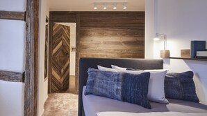 A bedroom with a wooden headboard, a bed with white and blue bedding, a bedside table with a lamp, and a wooden door with a herringbone pattern. - Bachofer (Waiblingen)