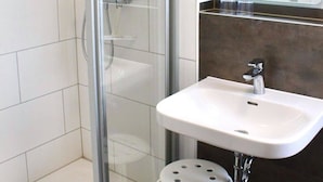 Un baño moderno con ducha de vidrio, un lavamanos blanco sobre encimera oscura y un espejo sobre el lavamanos.