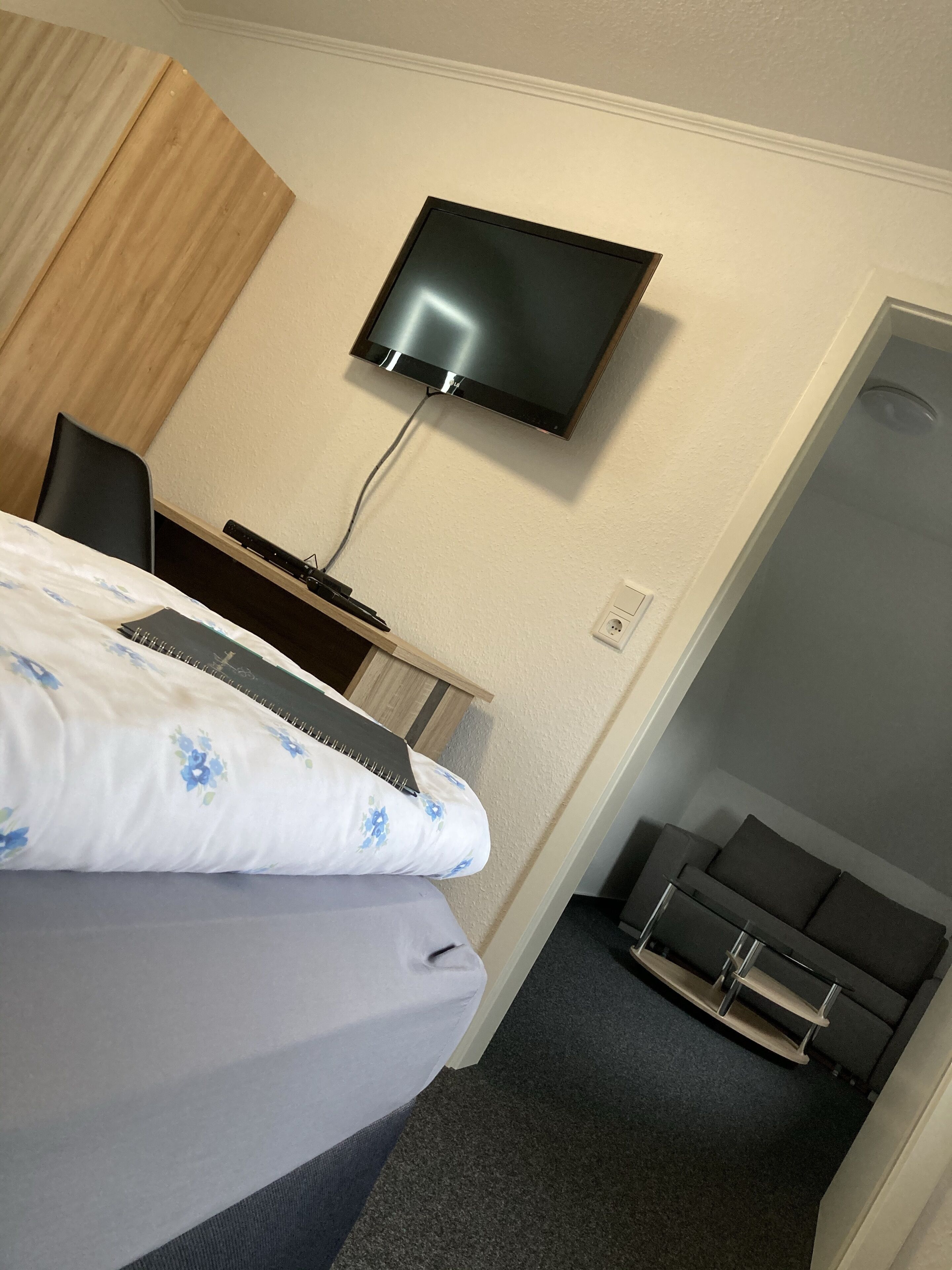 Une chambre d’hôtel comprenant un lit, un bureau avec un ordinateur, un téléviseur fixé au mur et un petit coin salon avec une chaise et un banc.