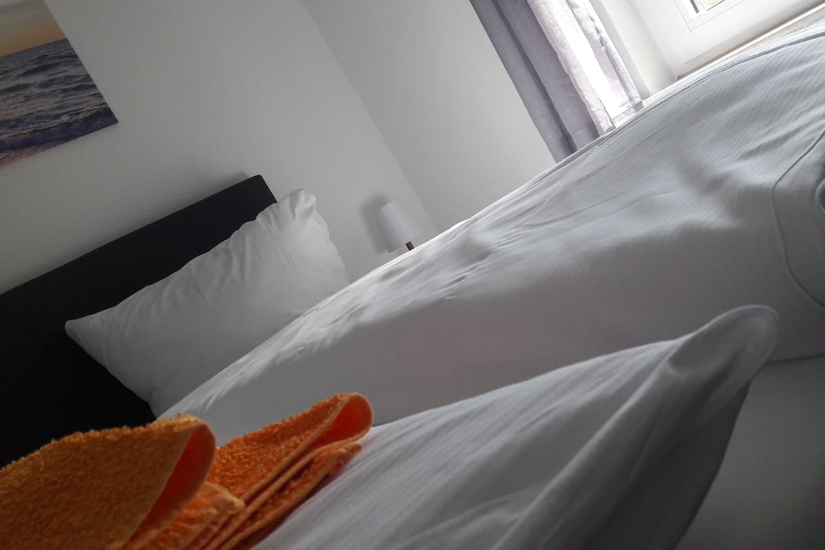 A hotel room with a bed, white linens, a black headboard, and an orange towel.
