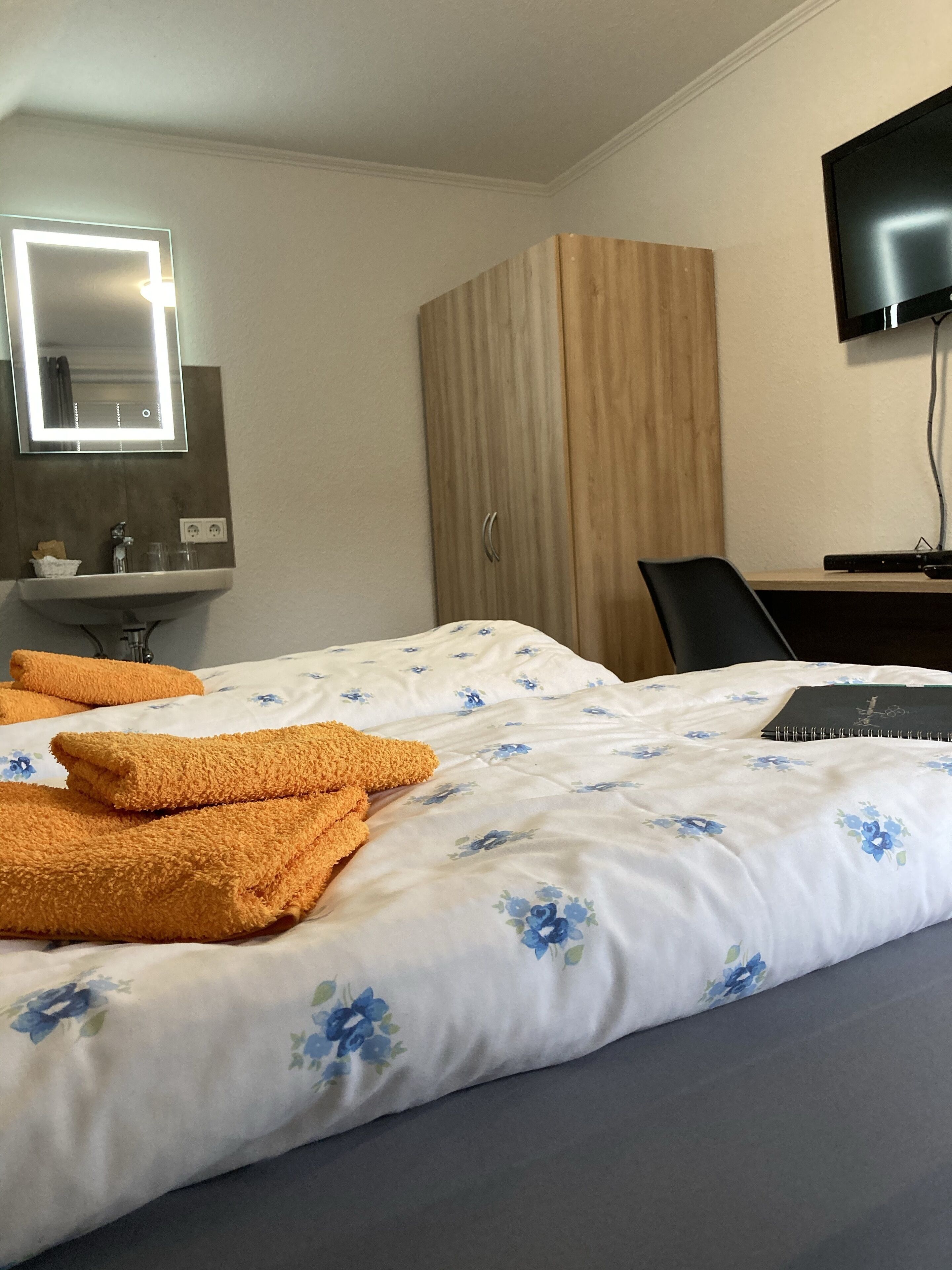 A hotel room with a bed, a desk, a TV, a wardrobe, and a bathroom with a mirror and sink.