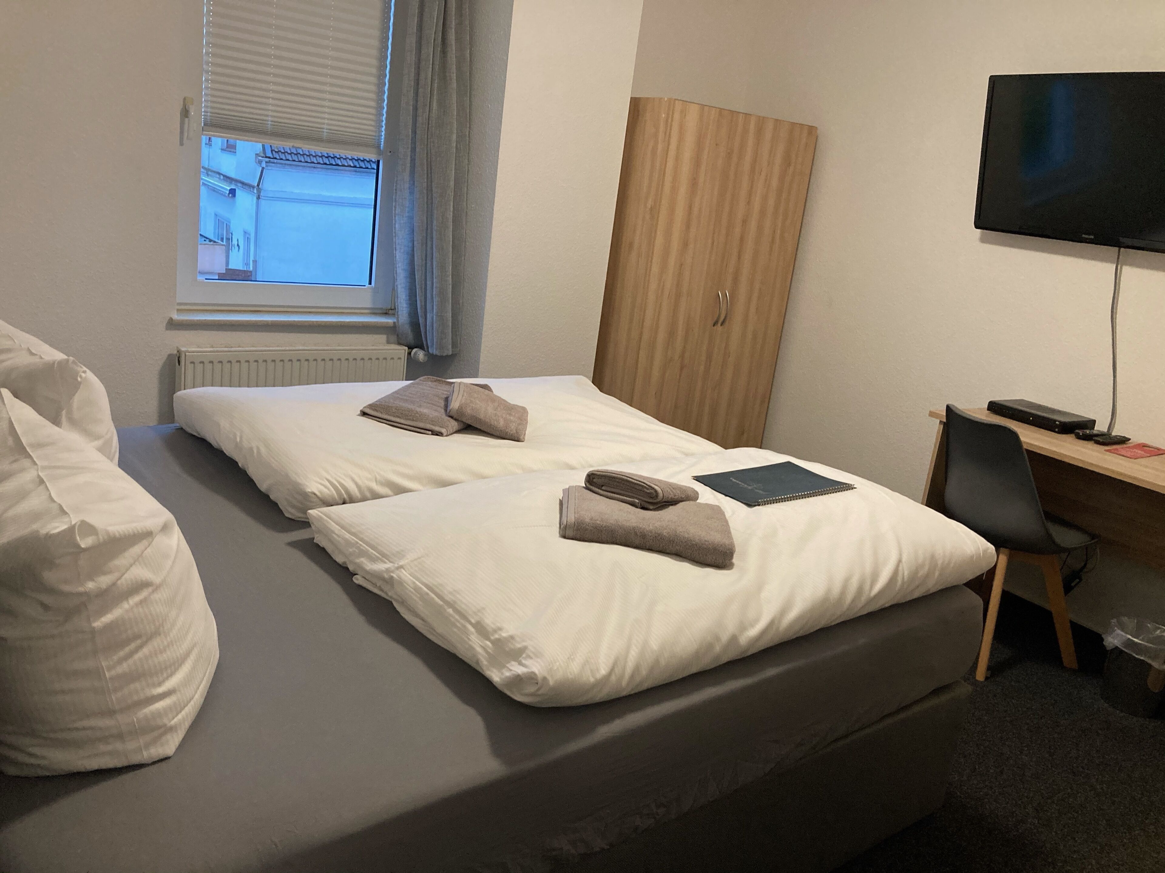 Ein Hotelzimmer mit zwei Betten, einem Holzschrank, einem Schreibtisch mit Computer und einem Fernseher.