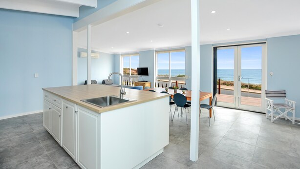 A modern kitchen with a large island, dining area with chairs, and a view of the ocean through large windows.