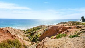A coastal landscape with a beach, rocky terrain, and sparse vegetation.