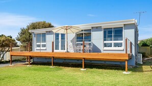 A modern house with a wooden deck, large windows, and an outdoor seating area with a table and chairs.