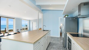 A modern kitchen with a large island, stainless steel appliances, and a view of the ocean.