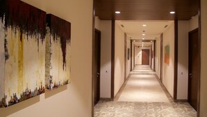 Ein Hotel-Flur mit Marmorboden, Holztüren und einem großen abstrakten Gemälde an der linken Wand.