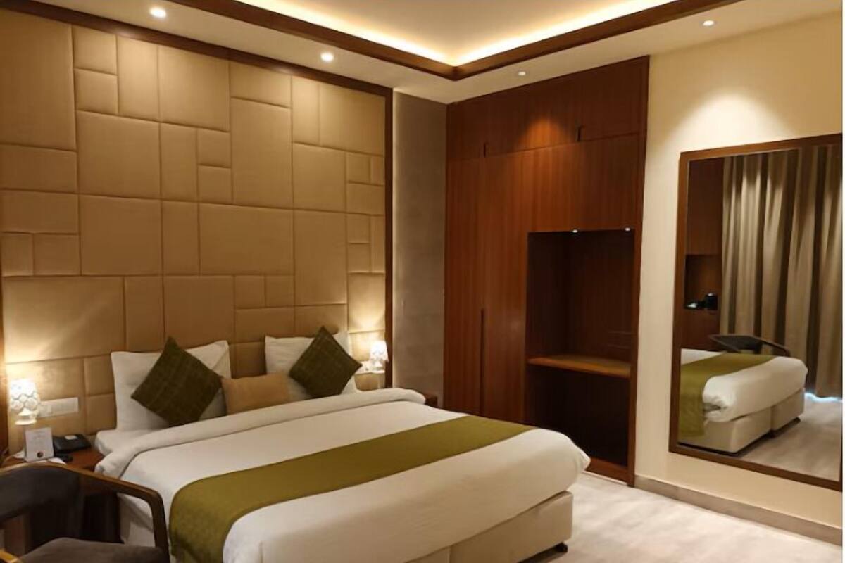 Habitación de hotel moderna con una cama grande, un armario de madera, un espejo y un escritorio pequeño con una silla.
