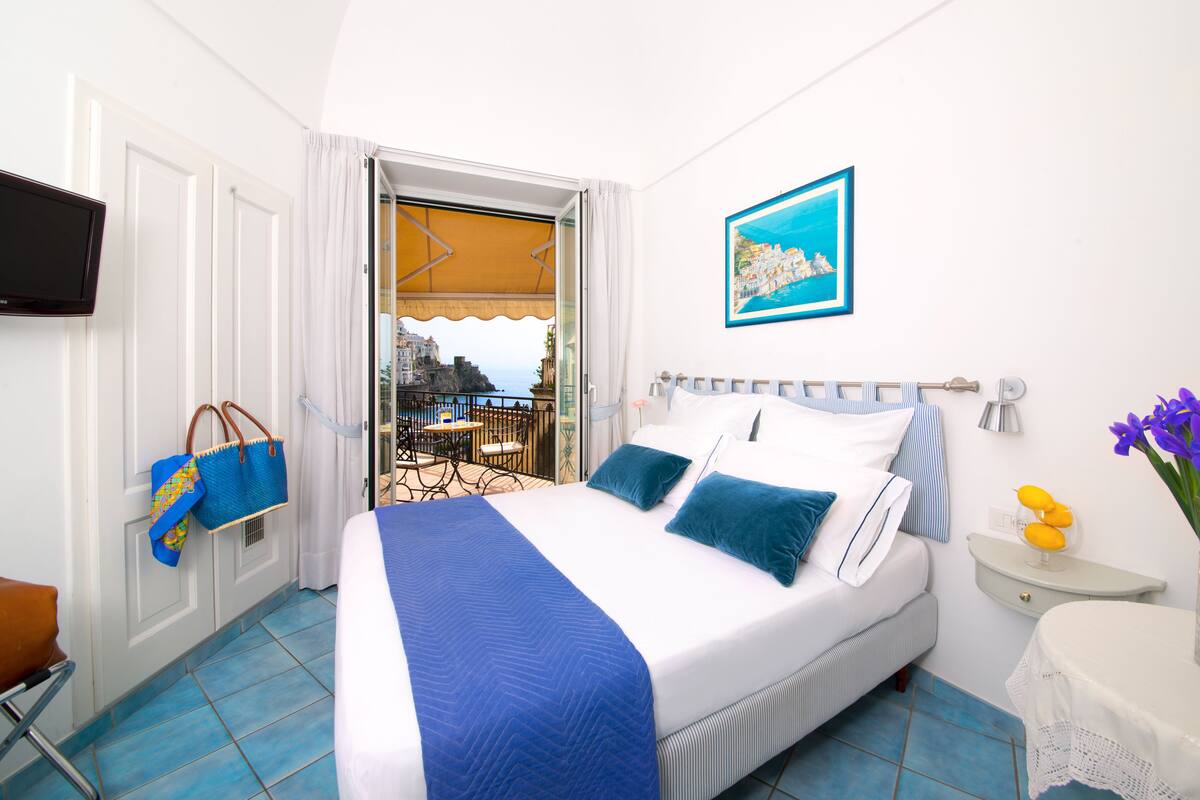 A hotel room with a bed, a TV, a balcony with a view, and a table with flowers.