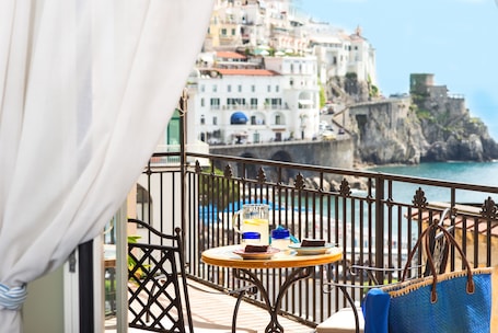 A balcony with a table set for two, overlooking a coastal town with historic buildings.